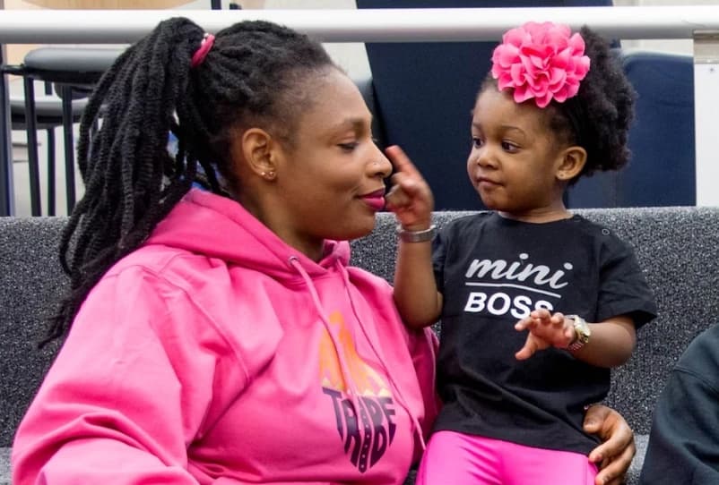 A mother in a pink hoodie sharing a playful moment with her young daughter